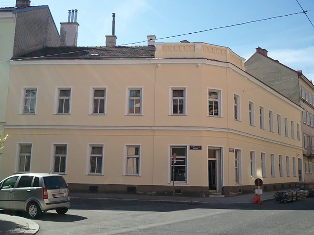 Eckhaus mit heller Fassde und weißen Fenstern, 2-stöckig, im 21. Bezirk von Wien