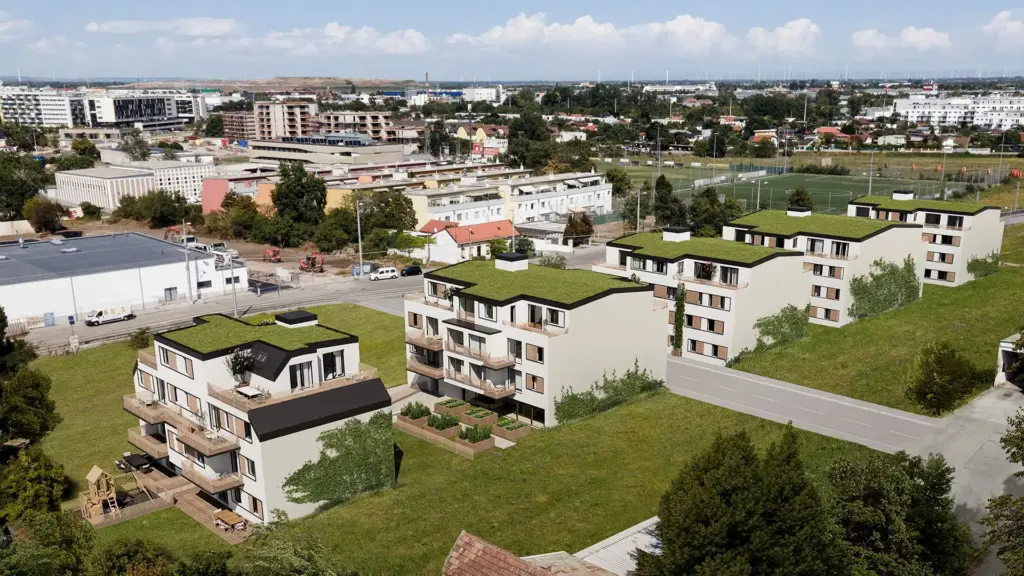 Blick über den 22. Bezirk von Wien, im Vordergrund eine moderne Wohnhausanlage mit fünf Gebäuden, helle Fassade und begrünten Dächern