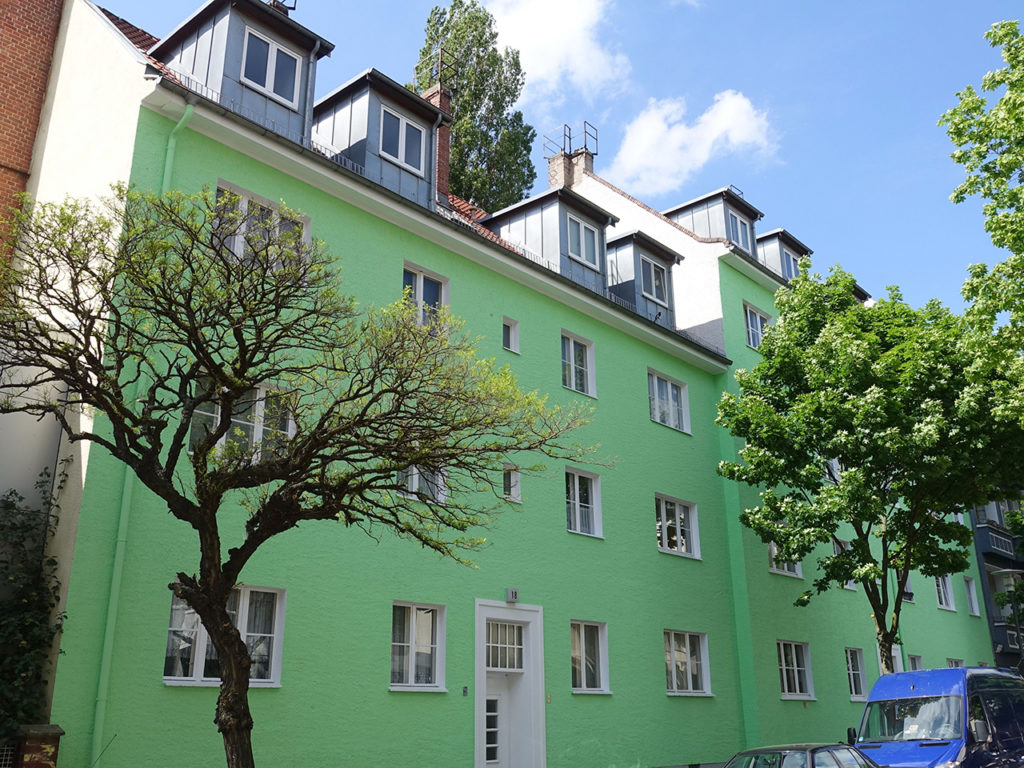 Wohnhaus mit Laubäumen davor, kräftig mintgrüne Fassade, weiße Fenster, in Berlin