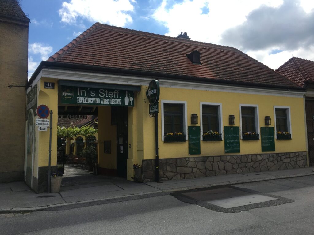 10. Bezirk von Wien, Lokal (Haus) mit großer Einfahrt, gelbe Fassade, dunkle Fenster, Straßenseitenblick