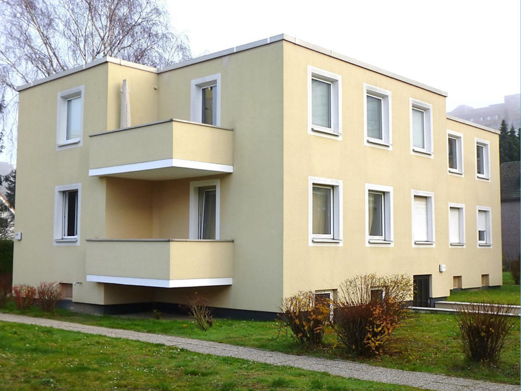 Wohnhausanlage in Berlin, 2-stöckig, gelbe Fassade, weiße Fenster und zwei Eck-Balkone