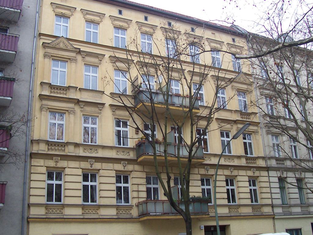 Zinshaus in Berlin, gelbe Fassade und weiße Fenster, Baum ohne Blätter im Vordergrund