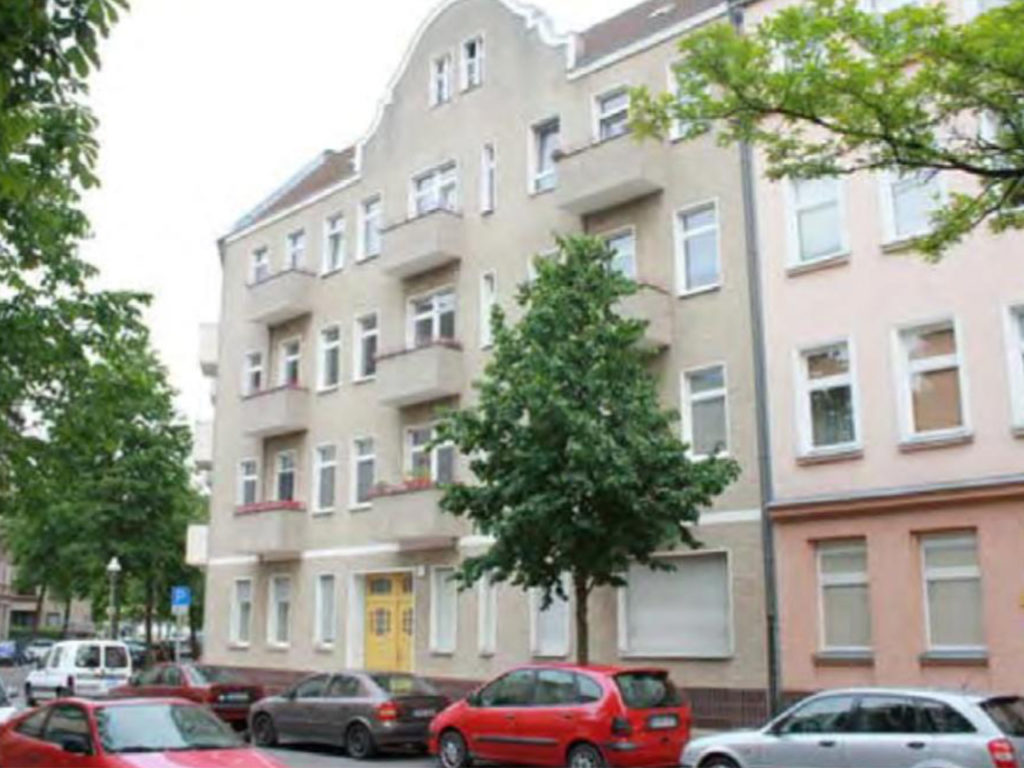 Eckzinshaus in Berlin, mit Balkonen und beige/grauer Fassade, Baum davor