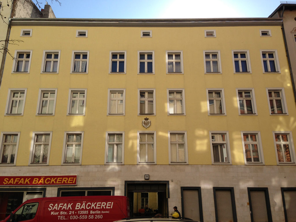 größeres Zinshaus mit gelber Fassade und Geschäftslokal im Erdgeschoß, Berlin