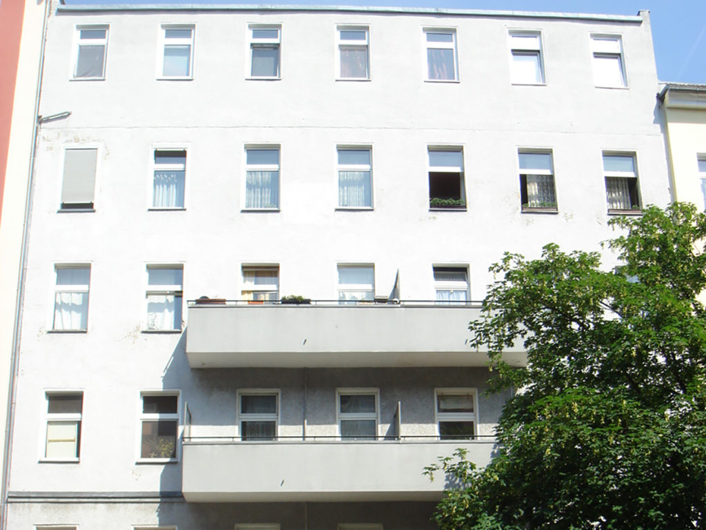 älteres Wohnhaus in Berlin, weiße Fassade und weiße Fenster, je ein Balkon in den unteren Geschossen