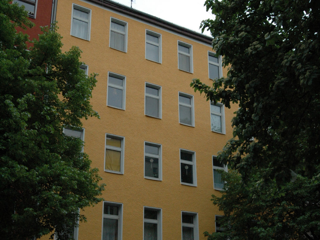 schlichtes mehrstöckiges Wohnhaus in Berlin, dunkelgelbe Fassade, weiße Fenster