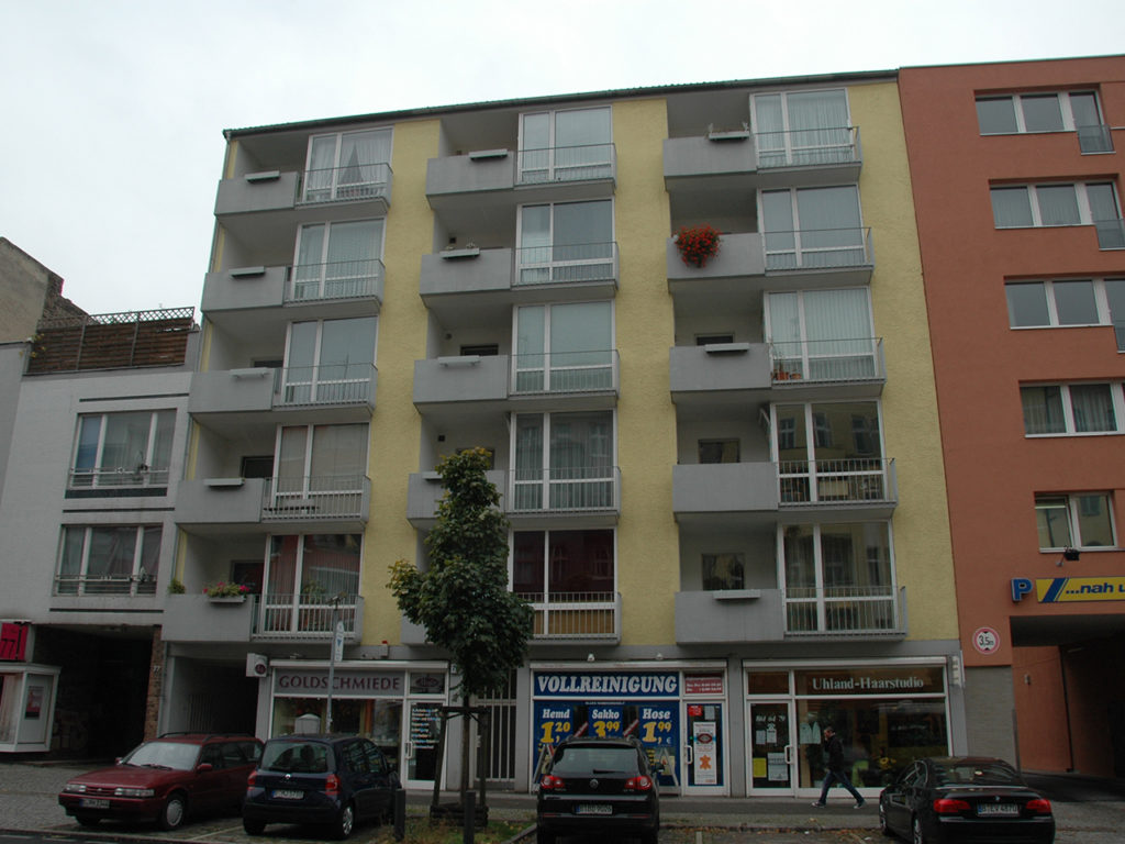 mehrstöckiges Wohnhaus mit gelber Fassade und grauen Balkonen, Geschäftslokale im Erdgeschoß, in Berlin