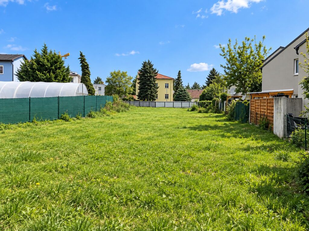 längliches Grundstück mit grüner Wiese, rechts und im Hintergrund Häuser
