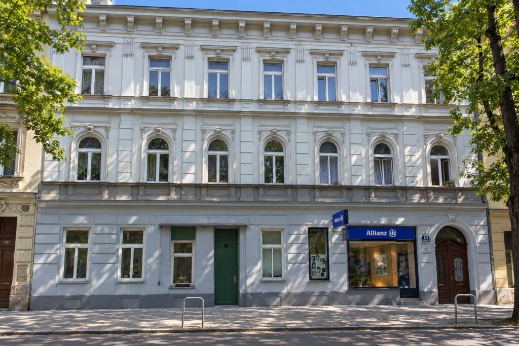 Zinshaus mit hellgrauer Fassade, links und rechts ein Baum
