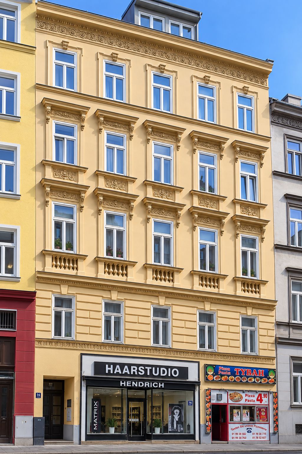 Zinshaus mit gelber Fassade, Fenster weiß, Gaupe, Geschäfte im Erdgeschoss