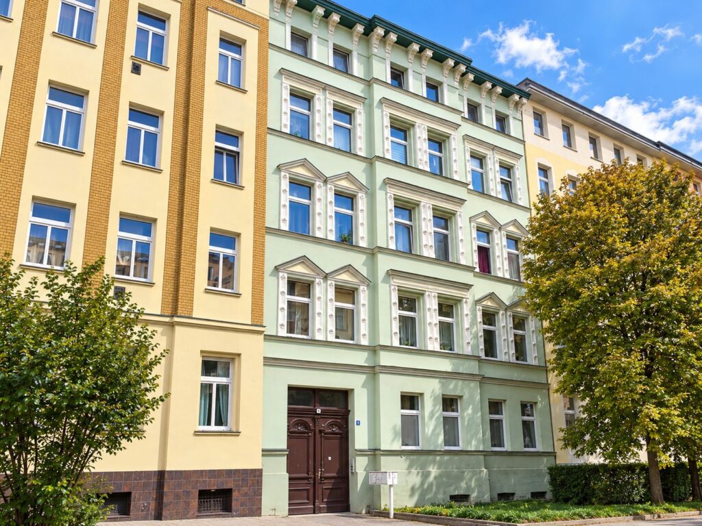 Zinshaus mit mintfarbiger Fassade, Fenster weiß, rechts ein Baum