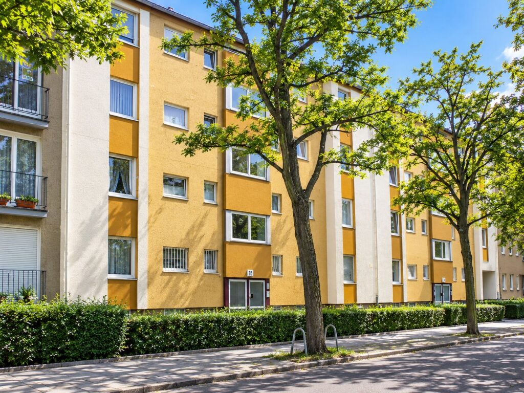 Wohnhausanlage mit gelber Fassade, weiße Fenster, Bäume