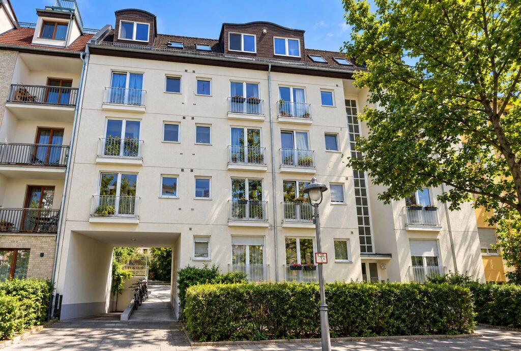 Wohnhausanlage mit hellgelber Fassade, französischen Balkonen, Baum und Straßenlaterne im Vordergrund