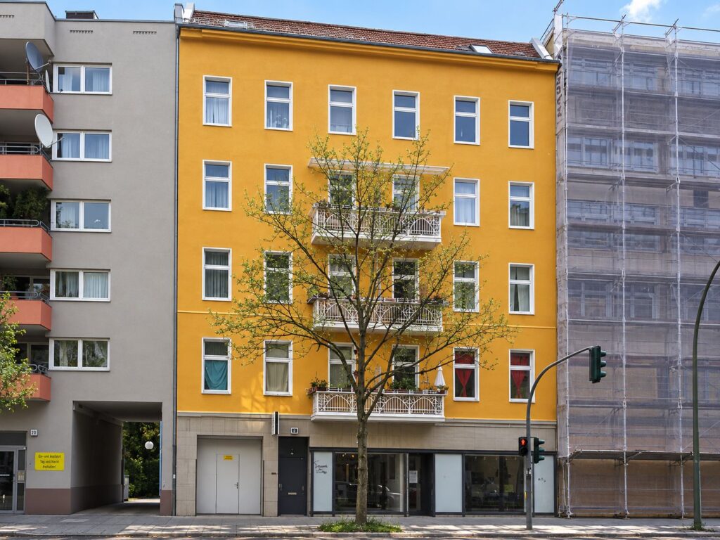 Zinshaus mit oranger Fassade, drei Balkonen, Fenster weiß, ein Baum davor