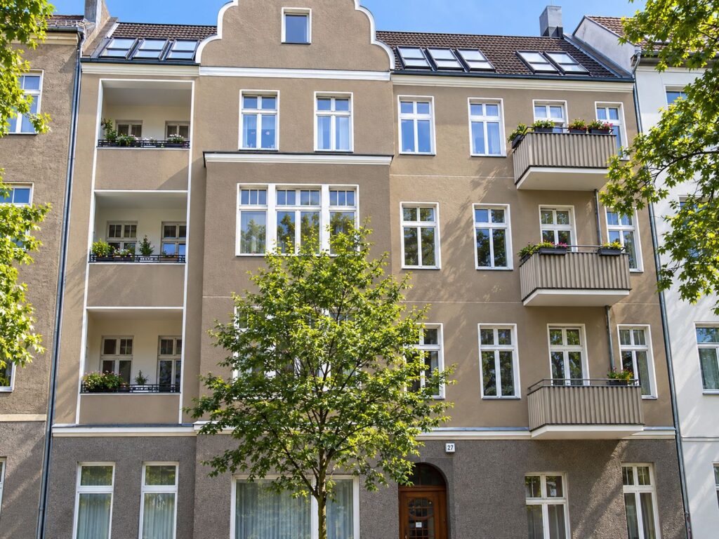 Zinshaus mit bräunlicher Fassade, weiße Fenster, Balkone, davor Bäume
